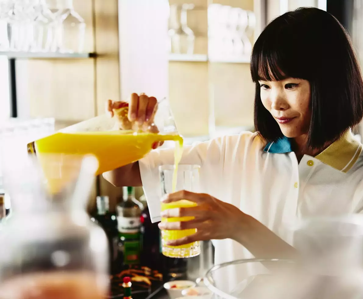 Womale bartender pouring a glass of orange juice.
