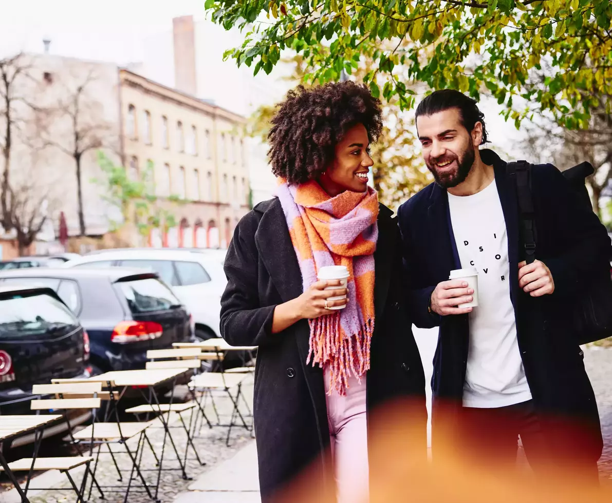 Smiling male and female having a conversation while holding drinks and walking outside.
