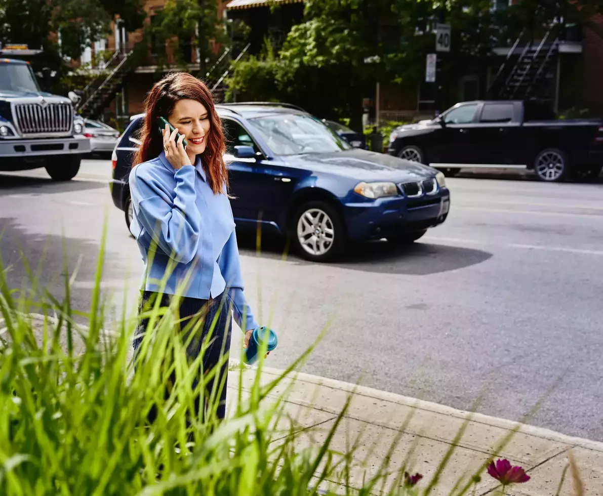 Female, talking on mobile phone, walking on sidewalk in busy street