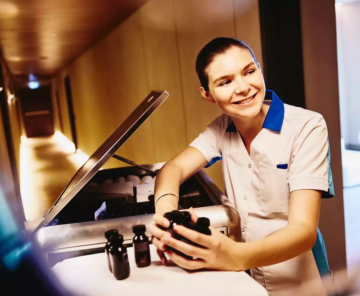 Womale in housekeeping uniform, holding small toiletries bottles.
