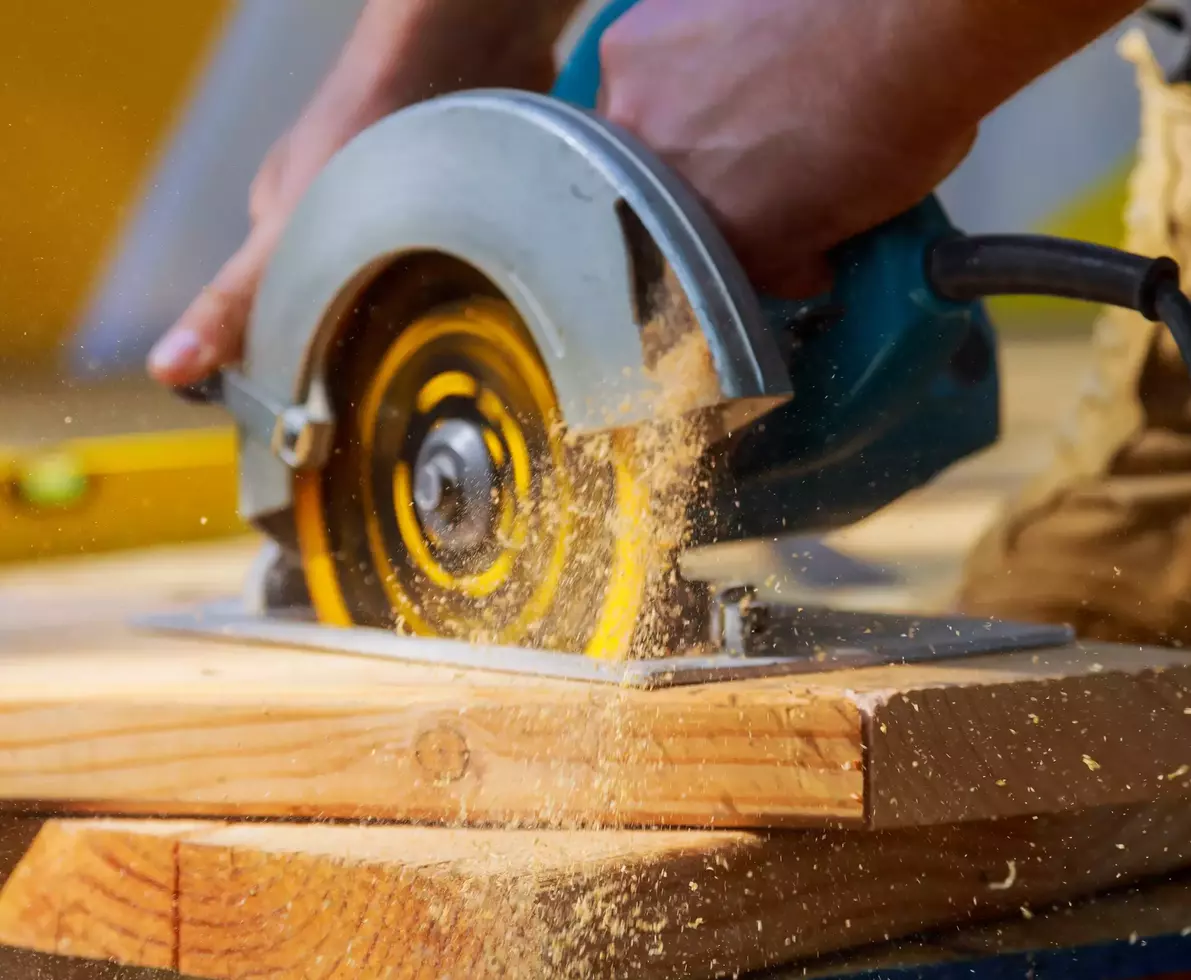 Carpenter using circular saw cutting wooden boards with hand power tools.