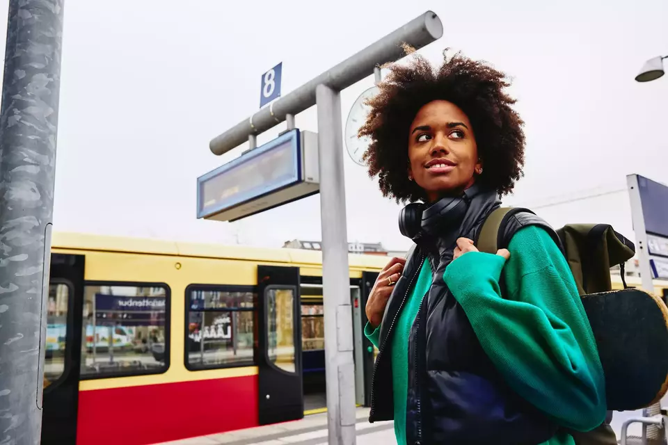 Smiling female, looking away on train platform. Train in background.
